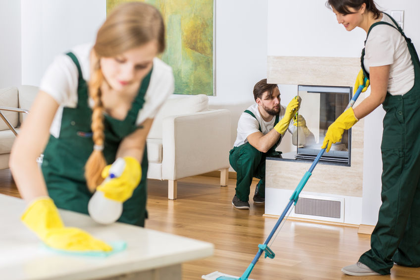 Three young professional cleaners in uniforms cleaning spacious living room